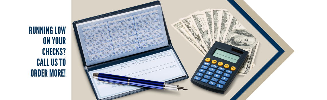 "An open checkbook with a pen, a calculator, and a stack of hundred-dollar bills. Text on the left reads 'Running low on your checks? Call us to order more!'"