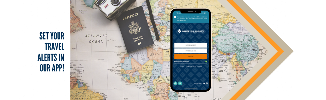 "A smartphone displaying the Bank & Trust Company app screen lies on a map, surrounded by a passport and travel documents. Text on the left reads 'Set Your Travel Alerts in Our App!'"