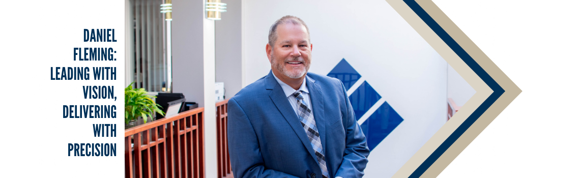Daniel Fleming, a professional man in a blue suit, smiling and standing in the Bank & Trust Company office. Text beside him reads: 'Daniel Fleming: Leading with Vision, Delivering with Precision.